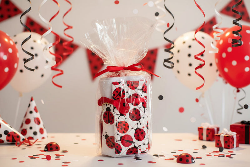 A gift-wrapped package featuring a white background with a red and black ladybug pattern, sealed in clear cellophane and tied with a red ribbon, on a light gray background.