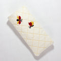 A quilted eyeglass case in cream with a yellow stitched diamond pattern and two embroidered ladybugs.